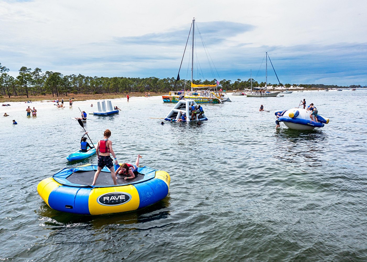 Shell Island Inflatable Adventure Park & Dolphin Sightseeing Tour-1 People enjoying water inflatables and paddleboarding near sandy beach